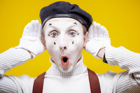 Portrait of an actor as a pantomime with white facial makeup showing expressive emotions on the yellow background indoorsの写真素材