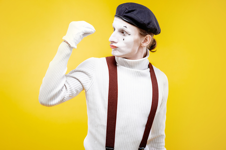 Portrait of an actor as a pantomime with white facial makeup showing expressive emotions on the yellow background indoorsの写真素材