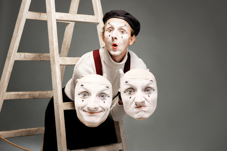 Portrait of a pantoomime actor holding facial masks in the studio with ladder on the grey backgroundの写真素材