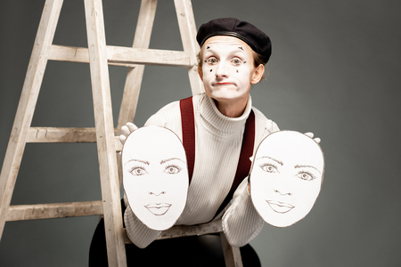 Portrait of a pantoomime actor holding facial masks in the studio with ladder on the grey backgroundの写真素材