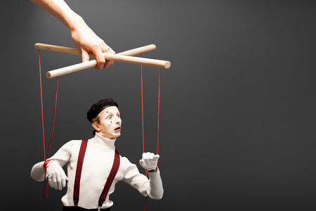 Actor as a marionette controlled with ropes by a huge hand on the grey background. Concept of a human controllingの写真素材