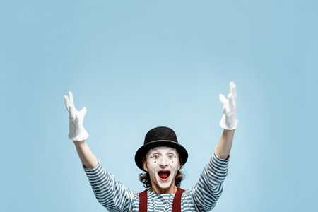 Emotional pantomime with white facial makeup showing empty space on the blue background, advertising somethingの写真素材