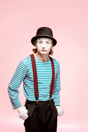 Portrait of an actor as a pantomime with white facial makeup posing with expressive emotions on the pink background indoorsの写真素材