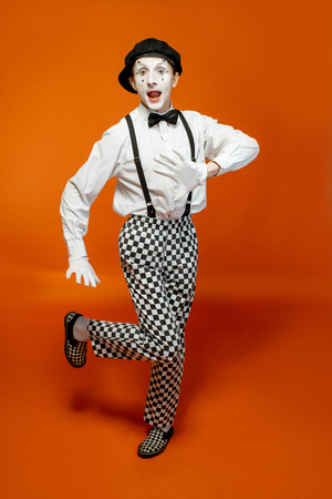 Full length portrait of an actor as a pantomime with white facial makeup showing expressive emotions on the orange backgroundの写真素材