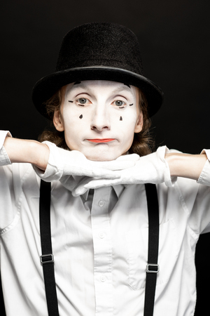 Close-up portrait of a pantomime with white facial makeup posing with expressive emotions on the black backgroundの写真素材