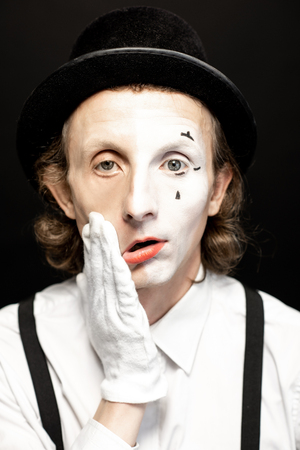 Portrait of a pantomime with a make-up on the one side of his face on the black background. Concept of a personality splitの写真素材