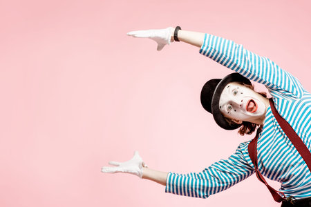 Emotional pantomime with white facial makeup showing empty space of the pink background, advertising somethingの写真素材