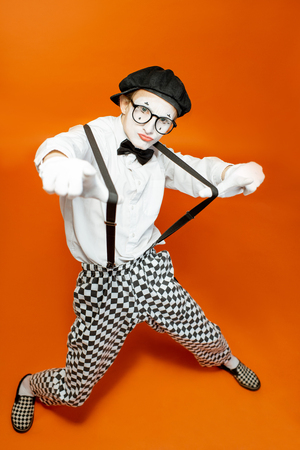 Portrait of an actor as a pantomime with white facial makeup showing expressive emotions on the orange background in the studioの写真素材