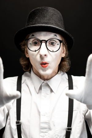 Close-up portrait of a pantomime with white facial makeup posing with expressive emotions on the black backgroundの写真素材