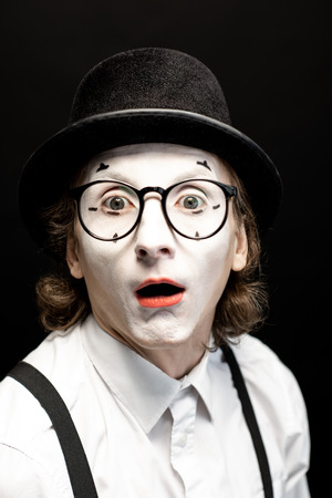 Close-up portrait of a pantomime with white facial makeup posing with expressive emotions on the black backgroundの写真素材