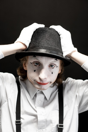 Close-up portrait of a pantomime with white facial makeup posing with expressive emotions on the black backgroundの写真素材