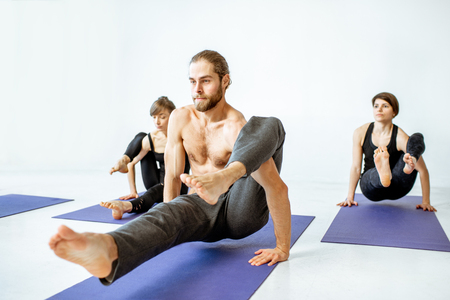 Group of young athletic people practising yoga during the lesson in the white fitness studioの写真素材