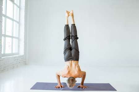 Senior athletic man with exposed torso practising yoga poses in the white studio
