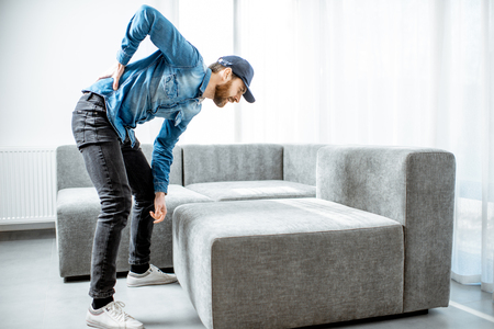 Delivery man suffering from the back ache while moving the couch in the apartmentの写真素材