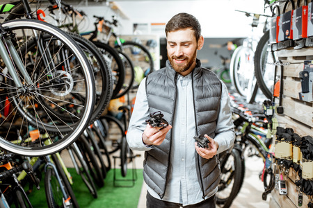 Man choosing bicycle parts standing in the store with lots of new bicycles on the backgroundの写真素材