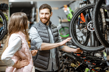 Salesman helping young woman to choose a new bicycle to buy standing in the bicycle shopの写真素材