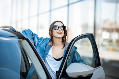Portrait of a young and happy woman standing near the modern car outdoors