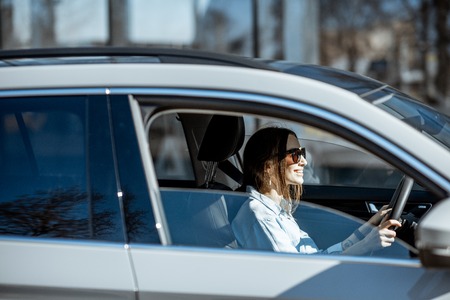 Young and happy woman driving luxury car in the city, side view through the door windowの写真素材