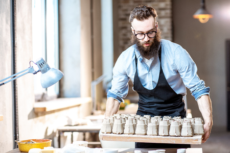 Handsome bearded man carrying tray with ceramic workpieces at the pottery shopの写真素材
