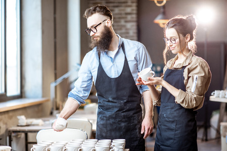Man and woman working with clay workpieces making ceramic products at the working place of the pottery shopの写真素材