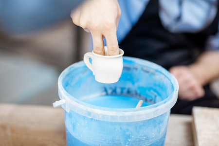 Painting clay jugs, diving into the bucket with blue paint, close-up viewの写真素材