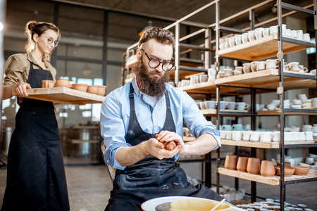 Handsome man in apron preparing clay while making jugs on the pottery wheel at the manufacturingの写真素材