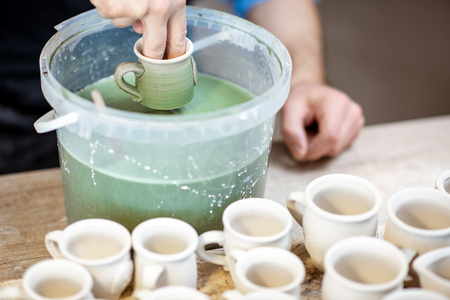 Painting clay jugs, diving into the bucket with blue paint, close-up viewの写真素材