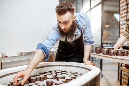 Man taking baked ceramic cups from the electric oven at the pottery manufacturingの写真素材