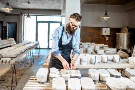 Handsome worker in apron getting clay products from the gypsum forms at the pottery manufacturingの写真素材
