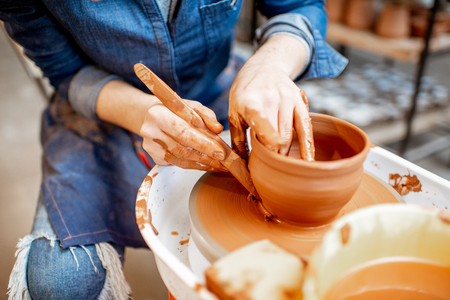 Woman making clay jug forming a shape with special tool on the pottery wheel, close-up viewの写真素材