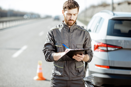 Road assistance worker in uniform signing some documents standing near the broken car on the highwayの写真素材