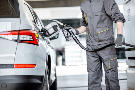 Gas station worker in workwear refueling luxury car with gasoline holding filling gun at the stationの写真素材