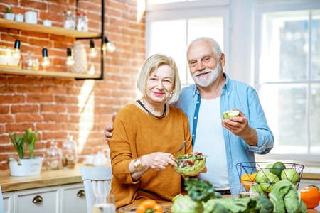 Portrait of a cheerful senior couple with salad and healthy food on the kitchen at home. Concept of healthy nutrition in older ageの写真素材