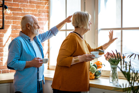 Grandparents waving hands and looking out the windowの写真素材