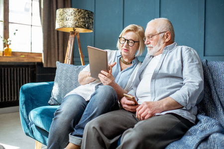 Lovely senior couple dressed casually using digital tablet while sitting together on the comfortable...