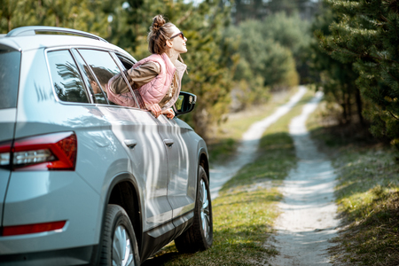 Young woman enjoying the trip, looking out the car window on a picturesque road in the woodsの写真素材