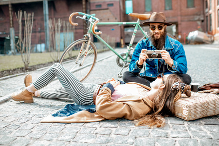 Stylish man photographing young woman lying on the street, having fun together on the urban backgroundの写真素材