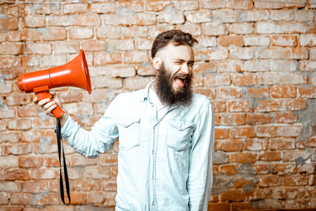 Handsome bearded man with red loudspeaker on the brick wall backgroundの写真素材