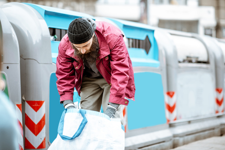 Homeless beggar searching somthing in the bag near the trash containers in the old cityの写真素材