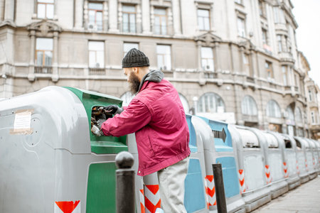 Homeless beggar searching glass bottles to surrender in the trash container at the city