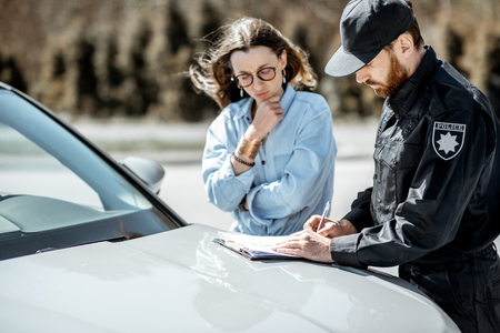 Policeman issuing a fine for violating the traffic rules to a young woman driver while standing near the car on the roadsideの写真素材