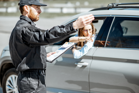 Policeman showing on the road sign while writing out fine for violation of traffic rules for a female driver on the city roadの写真素材