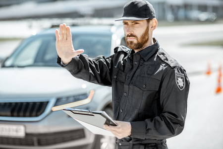 Portrait of a handsome policeman in uniform standing in front of a car on the roadsideの写真素材