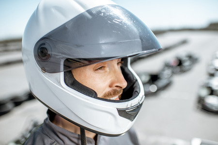 Close-up portrait of a male racer in protective helmet standing on the go-kart track outdoorsの写真素材