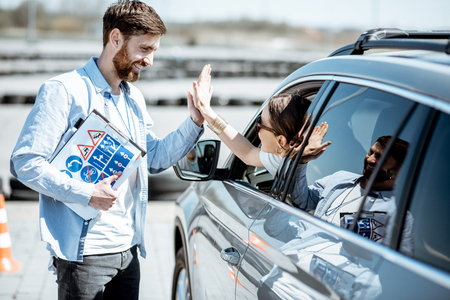 Instructor giving a five to a woman driver sitting in the car while learning to drive on the training groundの写真素材
