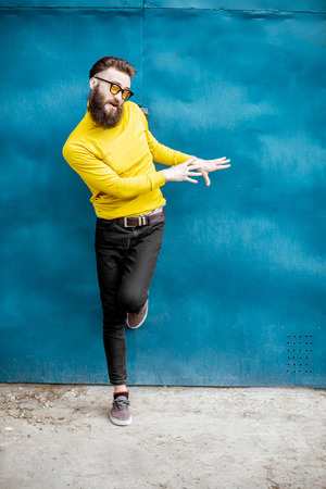 Full body portrait of a stylish bearded man in yellow sweater posing on the blue metal wall backgroundの写真素材