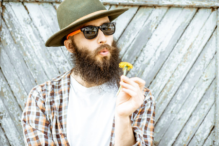 Portrait of a stylish man with flower and hat on the wooden gate background outdoorsの写真素材