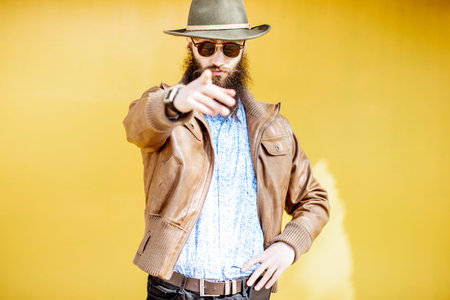 Portrait of a confident stylish man dressed in jacket and hat on the bright yellow background...