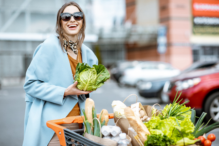 Young woman with shopping cart full of fresh and healthy food on the parking place near the supermarketの写真素材