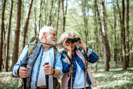 Beautiful senior couple hiking with backpacks and trekking sticks in the forest. Concept of active lifestyle on retirementの写真素材